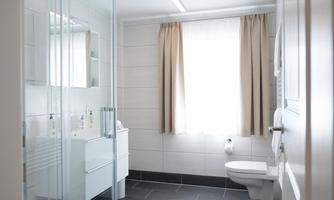 A modern bathroom with a shower, a sink, and a toilet. Light colors and large windows create a friendly atmosphere.