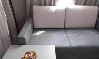 A cozy gray sofa with white cushions is placed in front of a bright window. On a small table lies a golden bowl with decorative elements.