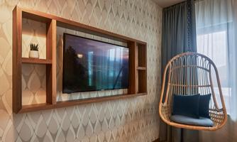 A modern living room with a television on the wall and a rocking wicker chair. The walls are decorated with a stylish pattern.
