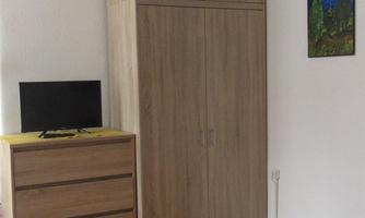 A simple bedroom with a bed, a television, and a wooden dresser. A small picture hangs on the wall.
