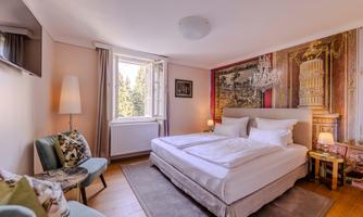 A cozy bedroom with a large bed and elegant decoration. The room has windows overlooking the outdoors and warm light.