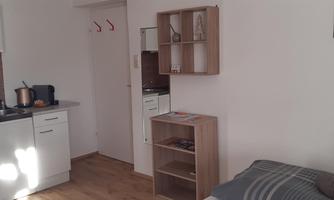 A cozy little apartment with a kitchenette and a living area. The walls are light and the floor is wooden, giving the space a friendly atmosphere.