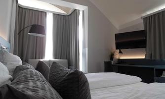 A modern bedroom with a comfortable bed and a cozy seating area. Large windows provide plenty of natural light and a relaxed atmosphere.