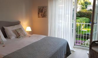 A comfortable room with a double bed and a balcony view of the garden. It is bright and inviting, featuring soft colors and cozy furniture.