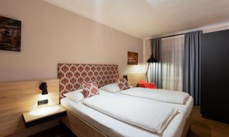 A modern bedroom with two single beds and stylish decor. Large windows let in a lot of light.