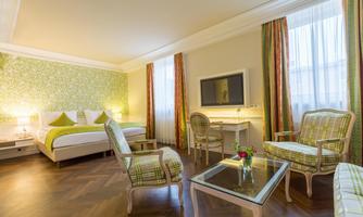 A modern hotel room with a cozy bed and stylish furniture. The walls are decorated with a green pattern and the room has large windows for plenty of daylight.