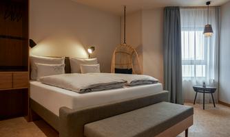 A modern bedroom with a large, comfortable bed and bright curtains. There is a cozy seating area and decorative lighting.