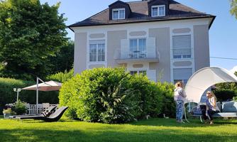 A beautiful house with a well-maintained garden. In the foreground, there are loungers and a seating area for relaxing.