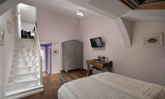 A cozy bedroom with a double bed and wooden flooring. A staircase leads to an upper area, and a television is mounted on the wall.