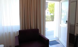 A modern room with a purple armchair and a large window pane. The door is open and lets in daylight.