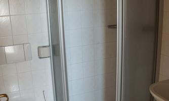 A simple bathroom with shower, toilet, and sink. The walls are tiled white and there is a clear, clean space.