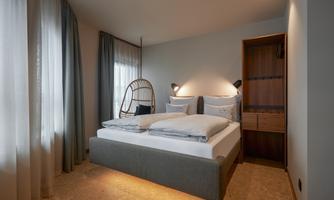 A modern bedroom with a large bed and stylish furniture. Bright curtains and soft light create a cozy atmosphere.