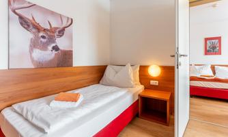 A simple room with a single bed and a cozy atmosphere.  
On the wall hangs a picture of a deer, and there is also a double bed in the background.