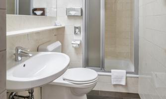 A modern bathroom with a sink, toilet, and a shower. The walls are lined with light tiles and the furnishings are simple and functional.