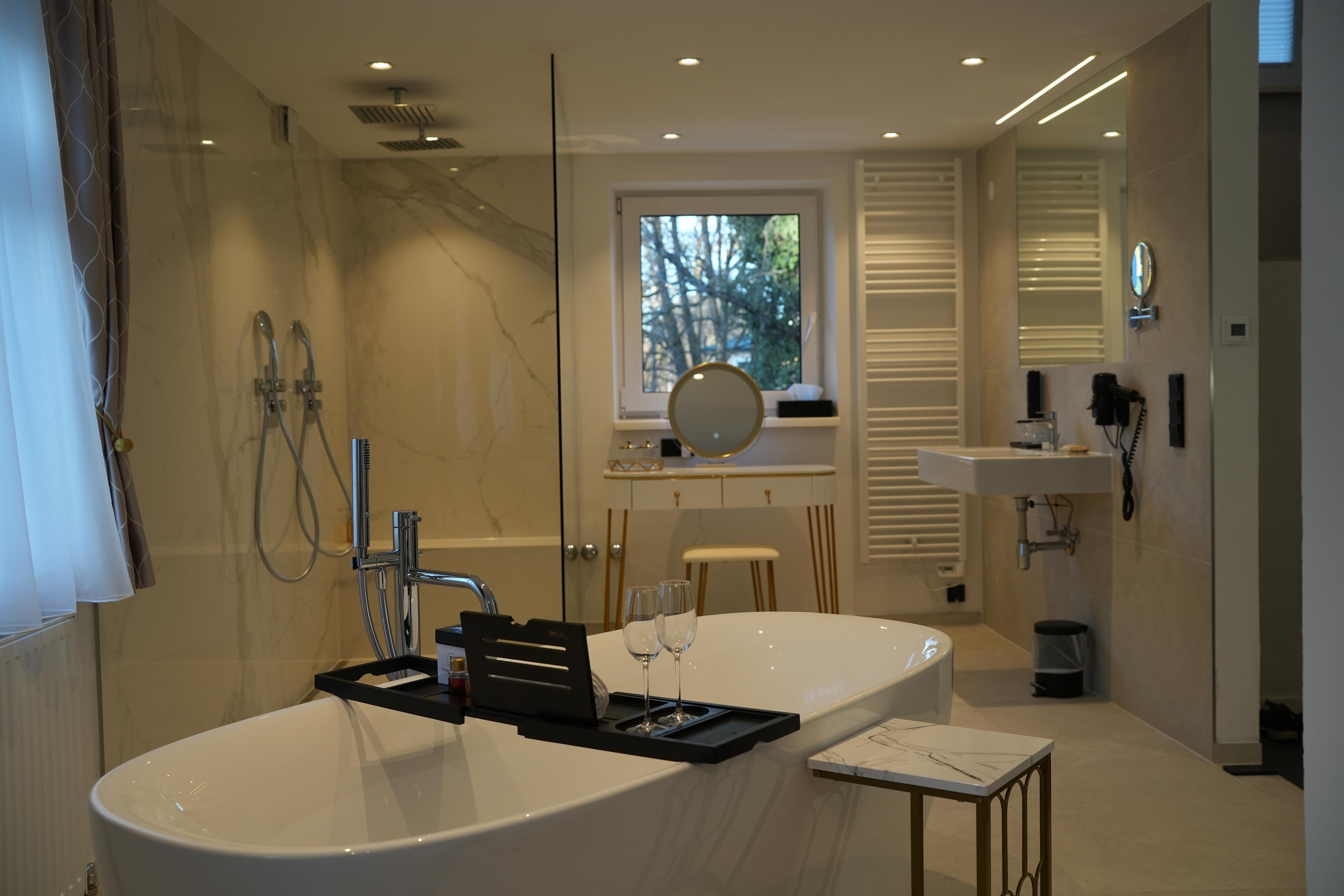 A modern bathroom with a freestanding bathtub and elegant fixtures. Large windows provide plenty of light and a pleasant atmosphere.