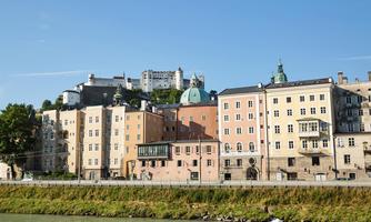 A picturesque city view with historic buildings by the river. In the background, a castle rises on a hill.