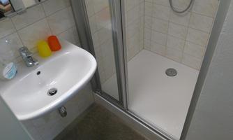 A modern bathroom with a sink and a shower. The walls are tiled and there are colorful soap dispensers on the sink.