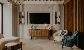 A modern furnished living room with a television on the wall. There is a combination of comfortable armchairs and a stylish wooden chest of drawers.