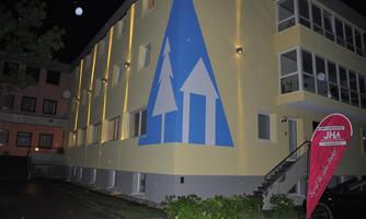 A modern building with a striking blue mural of trees. In the foreground, there is a sign with the JHA logo.