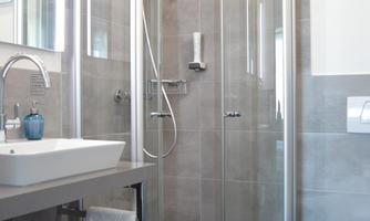 A modern bathroom with a glass shower and an elegant sink. The walls are in neutral shades, and there are clean towels on a shelf.