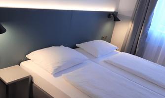 A modern bedroom with two single beds and soft lighting. The room has a pleasant color combination and a view of a window with curtains.