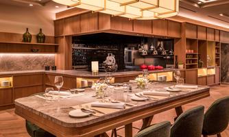 A modern restaurant with an elegant bar and a large dining table. The decor is stylishly designed with wooden and stone elements.