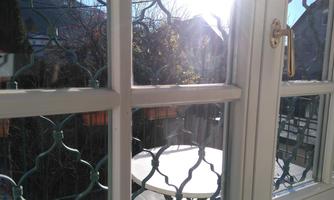 A view from a window with embossed glass. Outside, chairs and a table are visible, surrounded by trees and light.