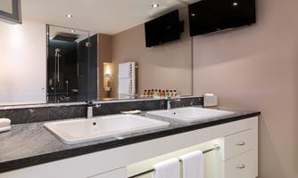 A modern bathroom with an elegant sink and plenty of storage space. Large mirrors and two televisions are mounted on the walls.