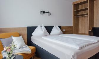 A modern bedroom with a large bed and two pillows. The decor is cozy and minimalist with a couch and a small table.