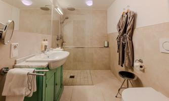 A modern bathroom with a green vanity cabinet. There is a shower, a large mirror, and two bathrobes hanging on a hook.