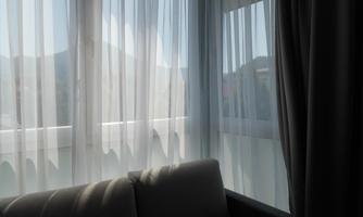 A bright room with translucent curtains. In the background, mountains and a balcony are visible.
