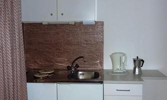A small kitchen corner with a sink, a kettle, and a coffee machine. The walls are kept in light colors, and the surfaces are simply designed.