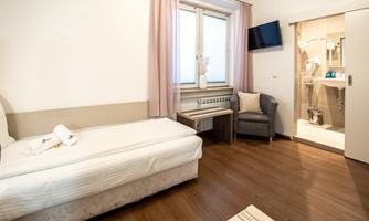 A simple hotel room with a single bed, a chair, and a table. The room has a television and a bathroom with a shower.