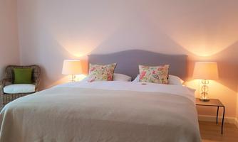 A cozy bedroom with a large bed and soft pillows. Gentle light from two bedside lamps creates a relaxed atmosphere.
