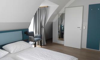 A bright bedroom with two beds and modern furniture. Large windows with curtains and a wall mirror give the room a friendly atmosphere.