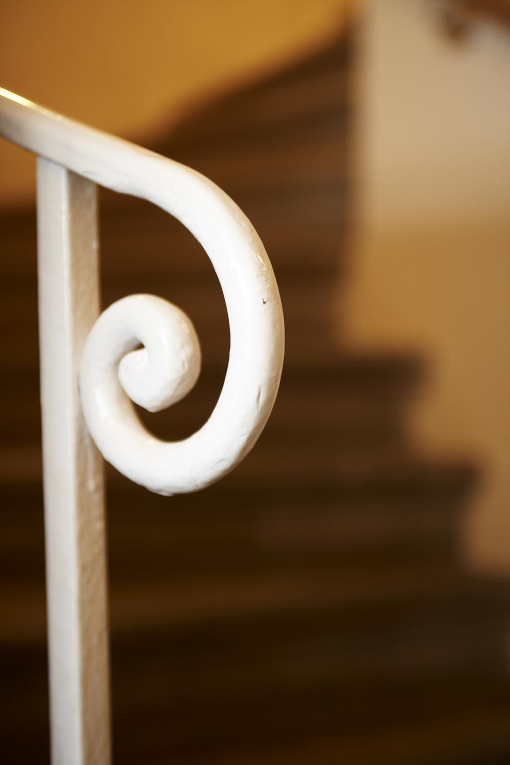 A curved, white railing detail with a staircase in the background. The steps are out of focus and rendered in neutral tones.