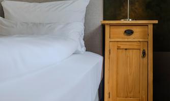 A stylish bedroom with a soft bed and a wooden nightstand. There is a lamp on the nightstand.