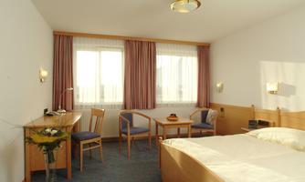 A cozy hotel room with a double bed and a seating area. Large windows provide plenty of light and a pleasant atmosphere.
