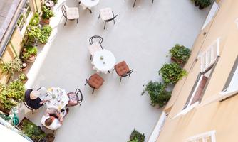 A cozy courtyard with tables and chairs, surrounded by plants. Two people are enjoying a meal in the open air.