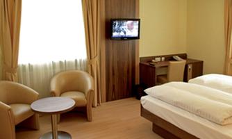 A modern hotel room with a double bed and a television. Two comfortable armchairs and a table complement the cozy furnishings.
