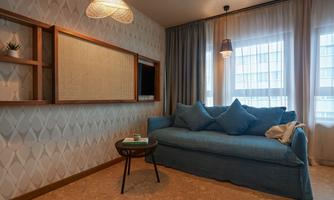 A modern living room with a blue sofa and large windows. The walls are decorated with an elegant pattern and the lighting is warm and inviting.