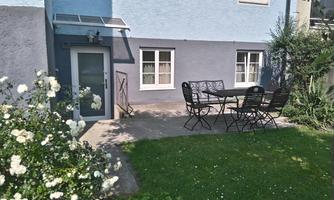 A cozy outdoor area with a table and chairs on the terrace. Surrounded by green grass and blooming roses.