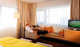 A modern hotel room with a cozy seating area and large windows. A person sits relaxed and enjoys the atmosphere.