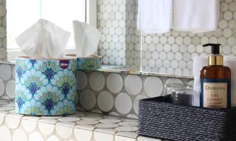 A stylish bathroom with a colorful tissue dispenser and a practical cosmetics shelf. The tiles are round and in soft colors.
