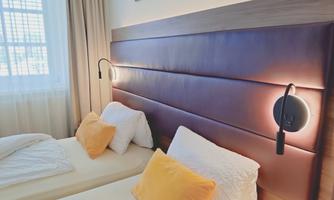 A modern bedroom with two single beds and elegant yellow cushions. The walls are bright and the lighting is warm and cozy.