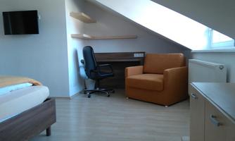 A modern room with a window, a desk, and a cozy armchair. A ceiling screen and a television complete the furnishings.