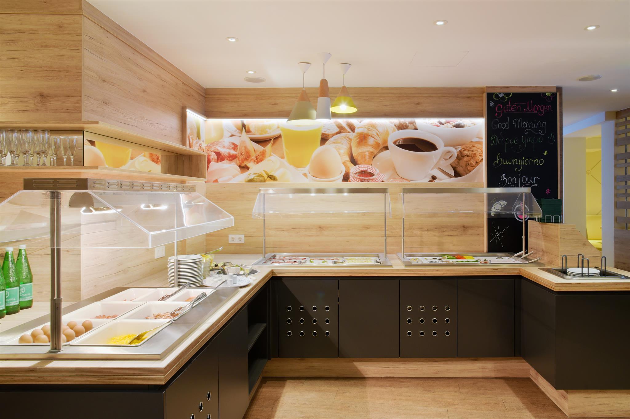 A modern buffet with wooden cladding and a selection of dishes. On the wall in the background, there are images of fresh breakfast and beverages.