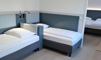 A modern room with two single beds and a minimalist design. The room is bright and friendly with a calm color scheme.