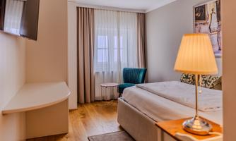 A modern bedroom with a large bed and a television on the wall. A cozy armchair and a beautiful view through the window create a pleasant atmosphere.