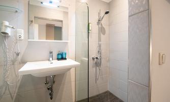 A modern bathroom with a shower and a washbasin. The walls are tiled in light colors and there is a mirror above the sink.